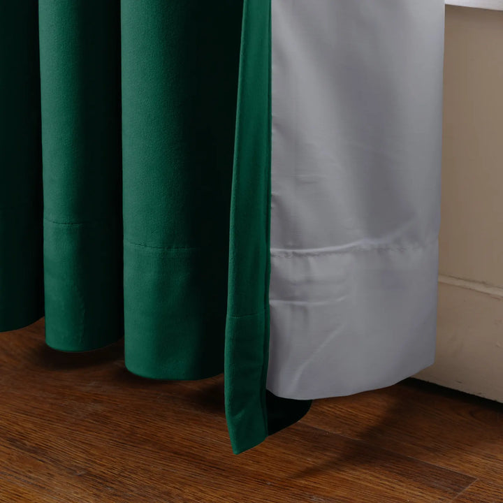 Close-up of dark green velvet curtain with white lining on wooden window sill.