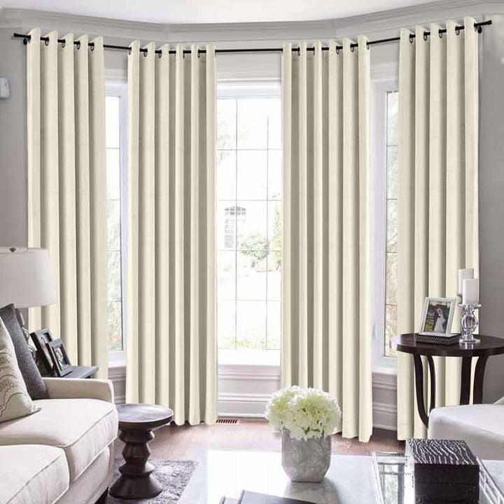 Beige grommet curtains in a bright living room with large windows and stylish white furniture.