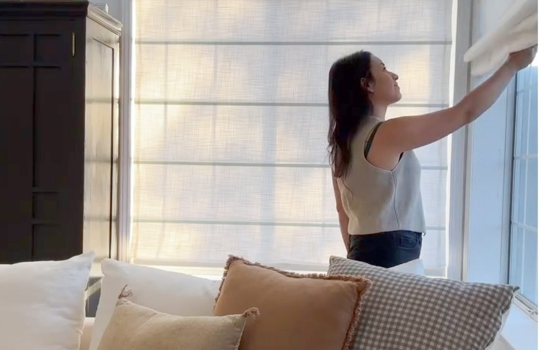 Woman adjusting a linen Roman shade, demonstrating its light filtering capabilities