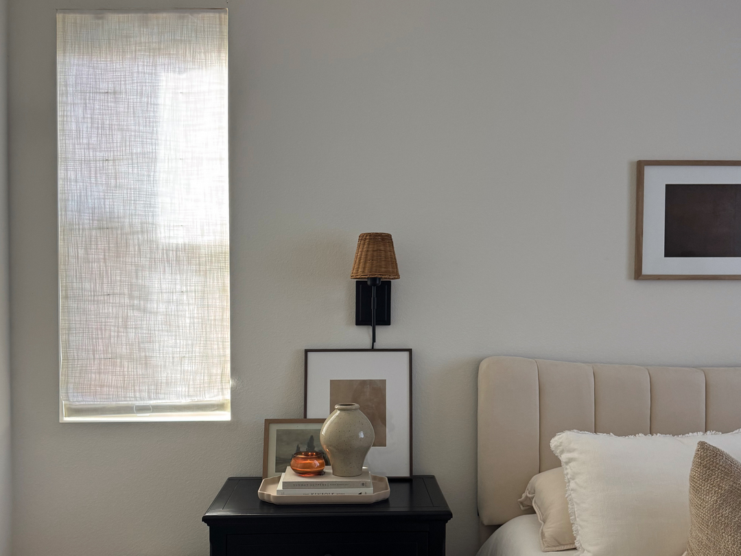 A bedroom with a bedside table next to a window featuring soft Hunter Douglas window treatments, creating a cozy ambiance